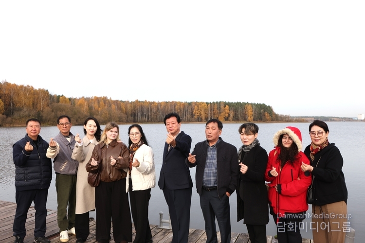 자슬라브스코예 호수(‘민스크 바다’)의 선착장에서 한국 대표단이 따뜻한 손하트 인사를 전하고 있다. 뒤로 펼쳐진 편백나무 숲이 황금빛 단풍으로 물들어, 호수의 잔잔한 수면과 어우러진 풍경이 마치 한 폭의 수채화를 닮았다. 늦가을 햇살 아래, 사람들의 미소와 자연의 빛이 함께 어우러진 순간이 벨라루스의 평화로움을 전한다.